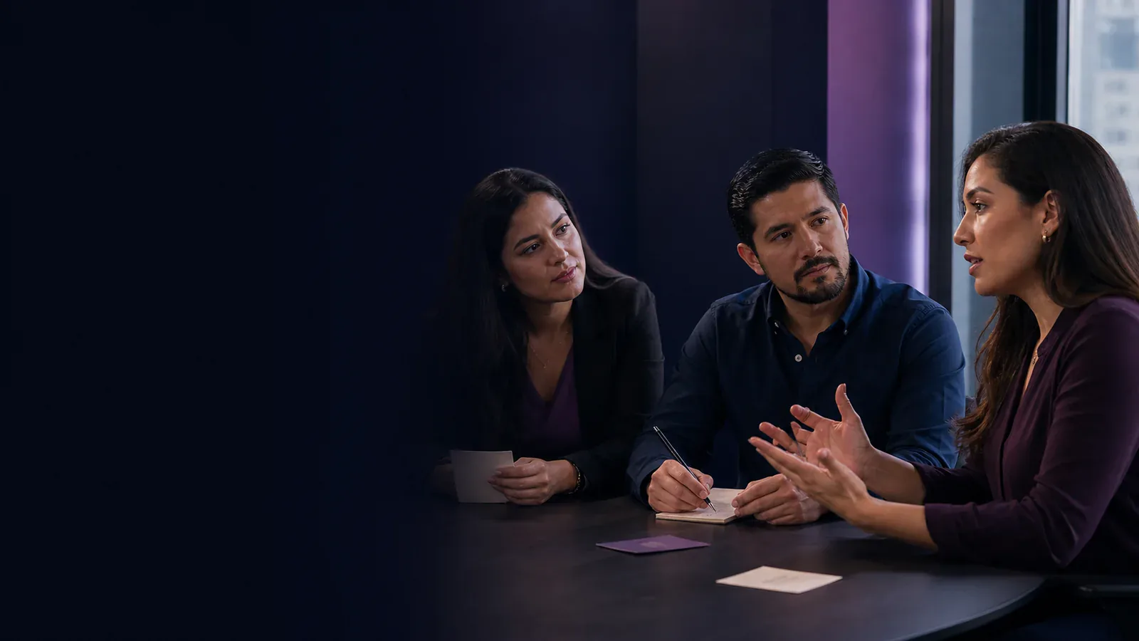 Tres profesionales latinoamericanos practican una conversación asertiva mientras escuchan, explican y toman notas.