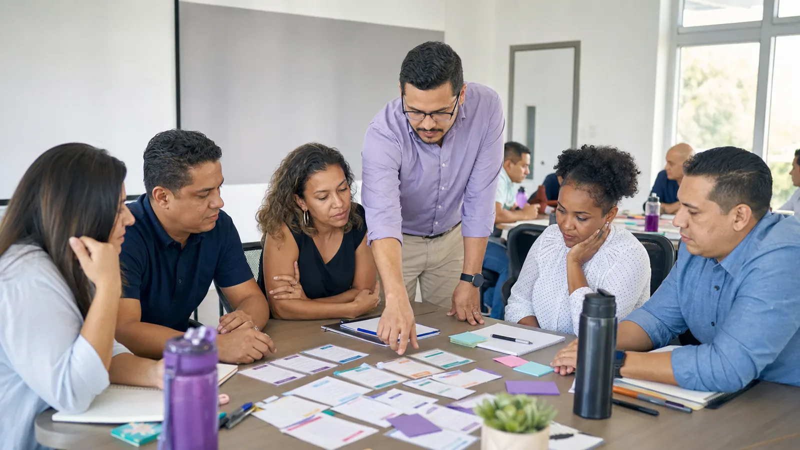 Un facilitador guía a un grupo diverso de personas adultas durante un taller práctico en equipo.