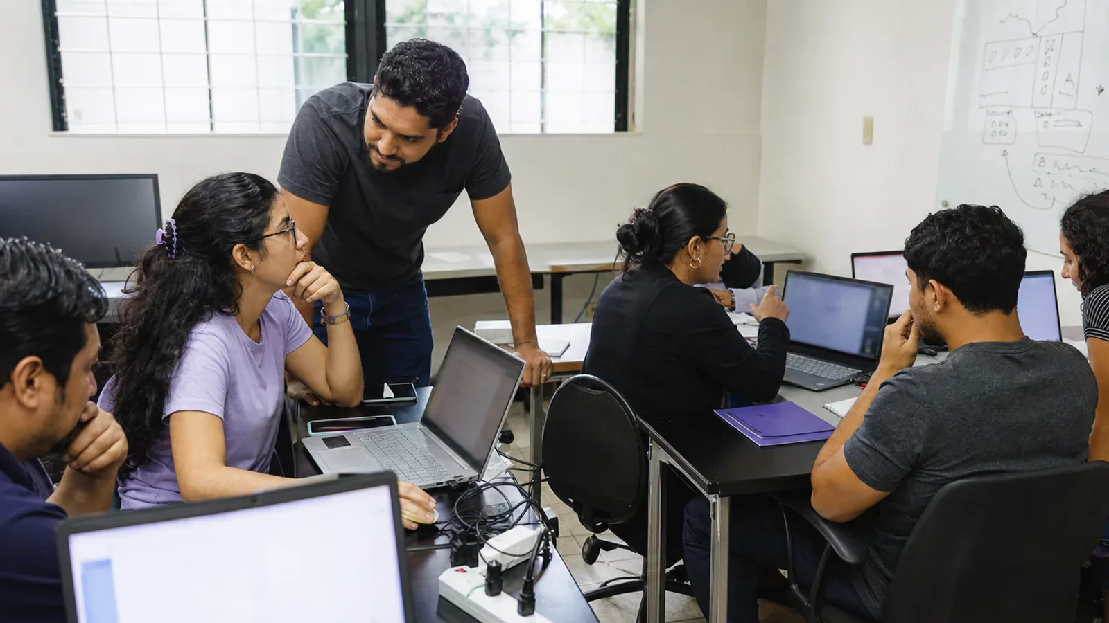 Un mentor de programación acompaña a dos grupos de estudiantes durante un laboratorio práctico.
