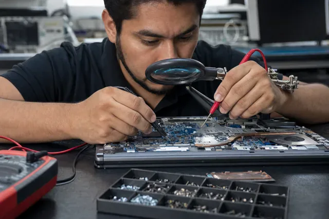 Technician measures an open laptop board with a multimeter.