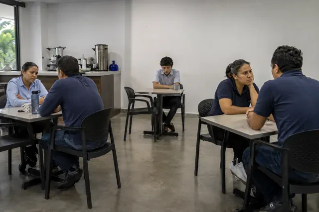 Employee remains isolated among tense groups in the staff dining area.