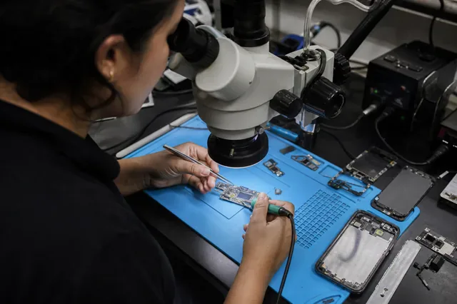 Technician repairs a disassembled phone board under a microscope.